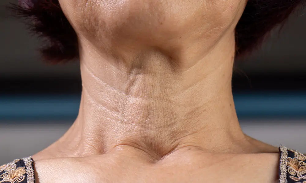 Woman applying skincare to natural neck skin with collagen capsules nearby