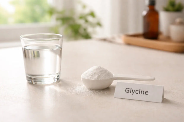 Glycine powder in a measuring spoon beside a glass of water on a minimalist bench.